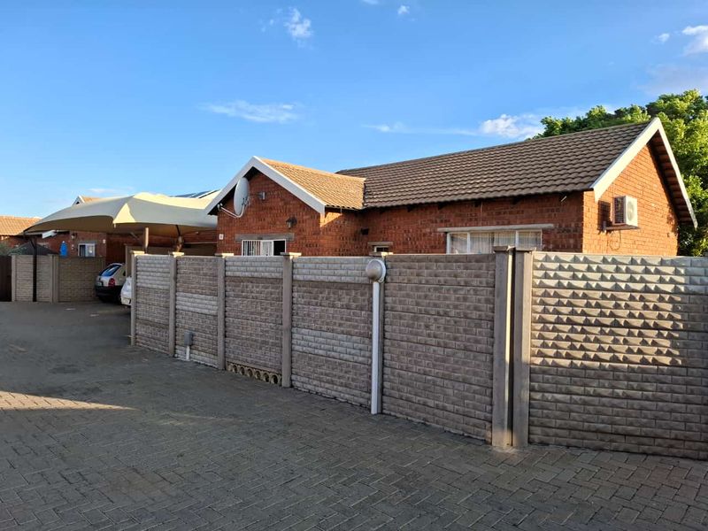Front view of a face brick townhouse featuring a tiled roof, paved driveway, and a secure precast concrete boundary wall.