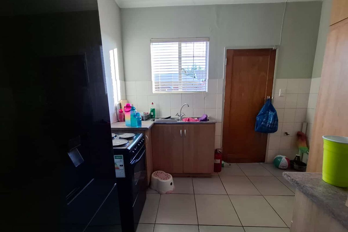 A functional kitchen featuring wooden cabinetry, tiled flooring, a stainless steel sink, and a tiled backsplash, offering potential for cosmetic updates.