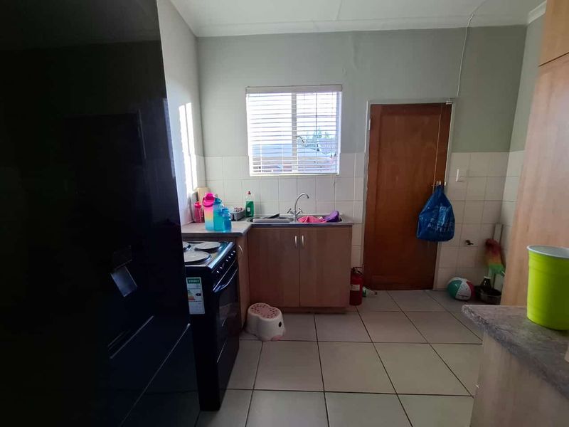 A functional kitchen featuring wooden cabinetry, tiled flooring, a stainless steel sink, and a tiled backsplash, offering potential for cosmetic updates.