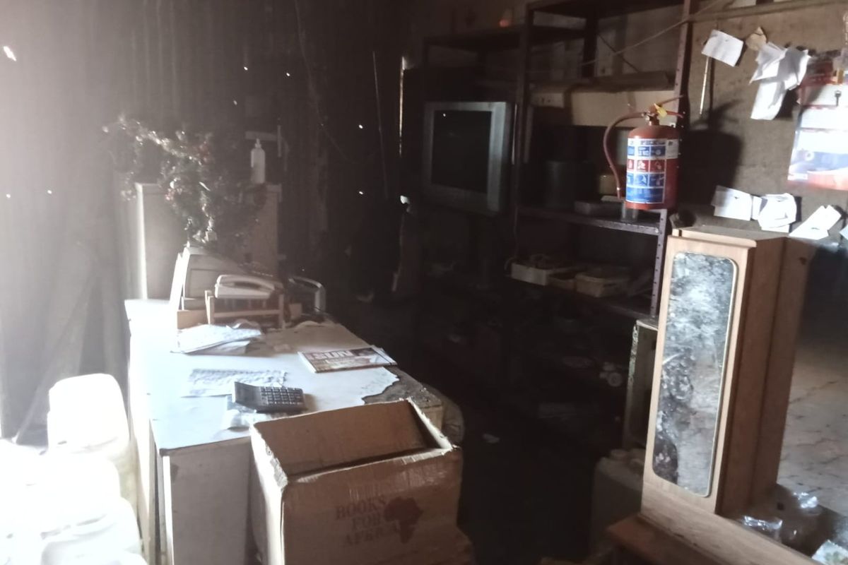 A dimly lit commercial office space featuring metal shelving and a fire extinguisher, currently in a state of significant disrepair and clutter.