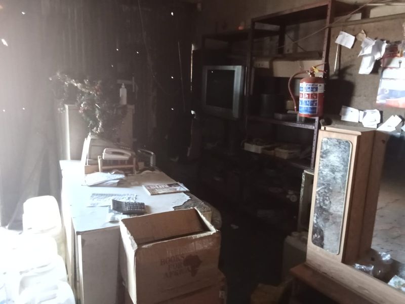 A dimly lit commercial office space featuring metal shelving and a fire extinguisher, currently in a state of significant disrepair and clutter.