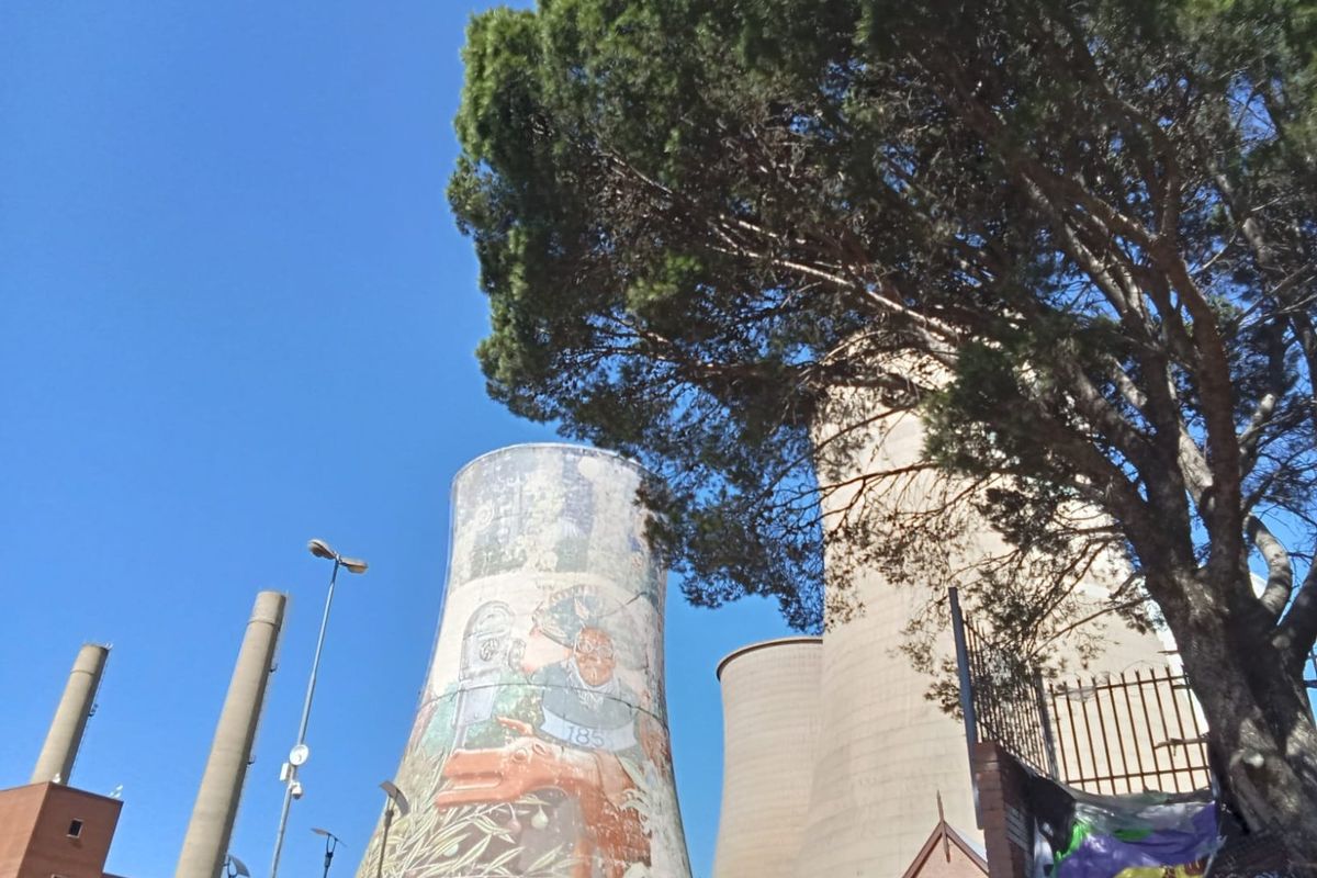 Exterior view of industrial cooling towers featuring a large mural, set within a fenced commercial site.