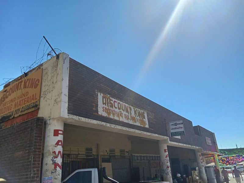 Commercial storefront featuring a brick facade, concrete support columns, and security gates, currently utilized for retail operations.