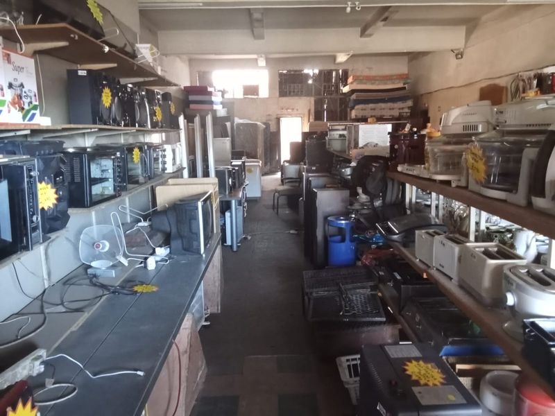 Commercial utility or storage space featuring exposed concrete beams, fixed wall shelving, and concrete flooring, currently utilized for retail inventory storage.