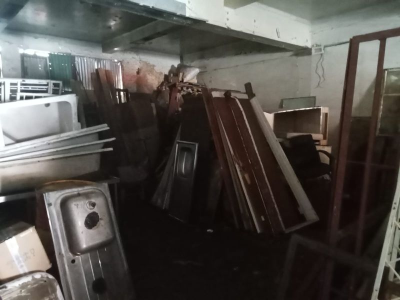 A cluttered utility or storage area featuring exposed concrete ceilings and masonry walls, currently used for storing various building materials and fixtures.