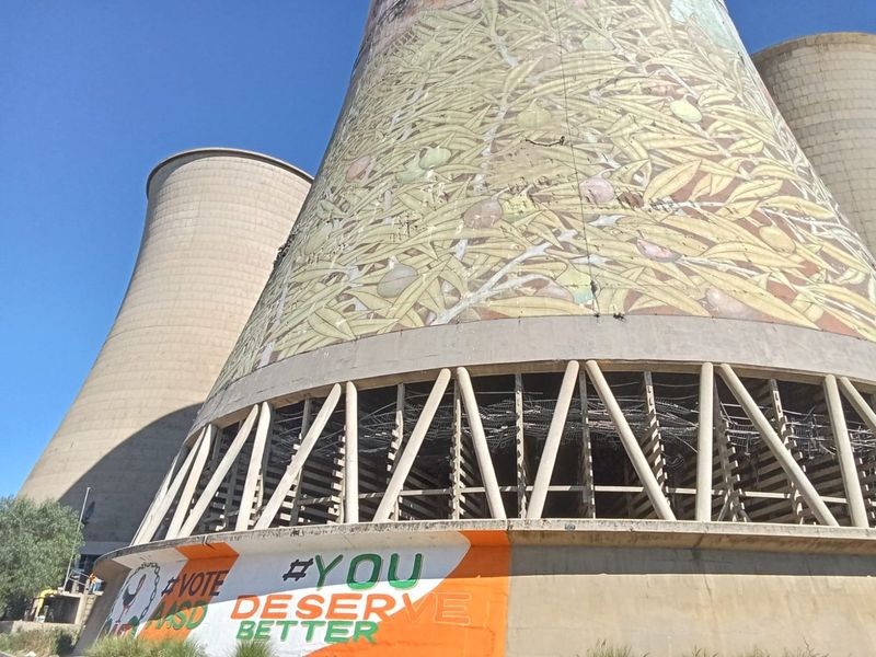 Large industrial cooling towers featuring a decorative mural and visible concrete structural supports, showing signs of weathering and age.