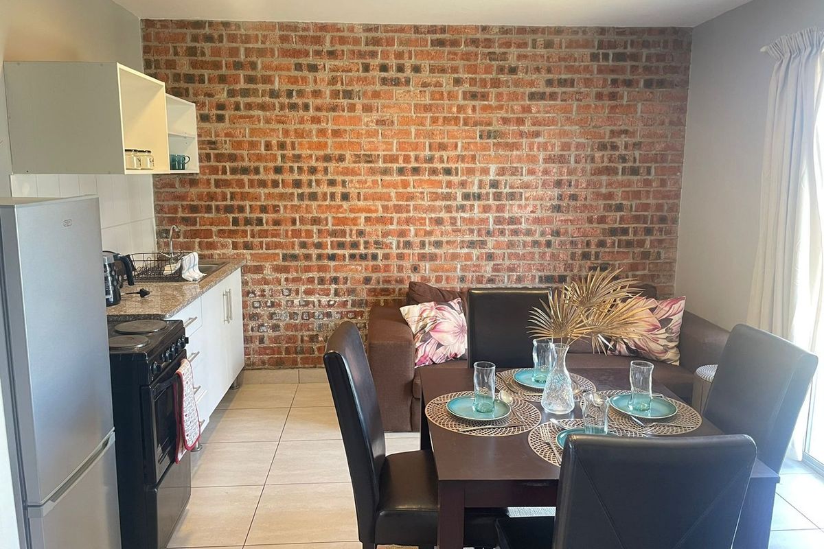 Open-plan living and kitchen area featuring a prominent exposed brick wall, tiled flooring, and functional kitchen cabinetry with a freestanding stove.