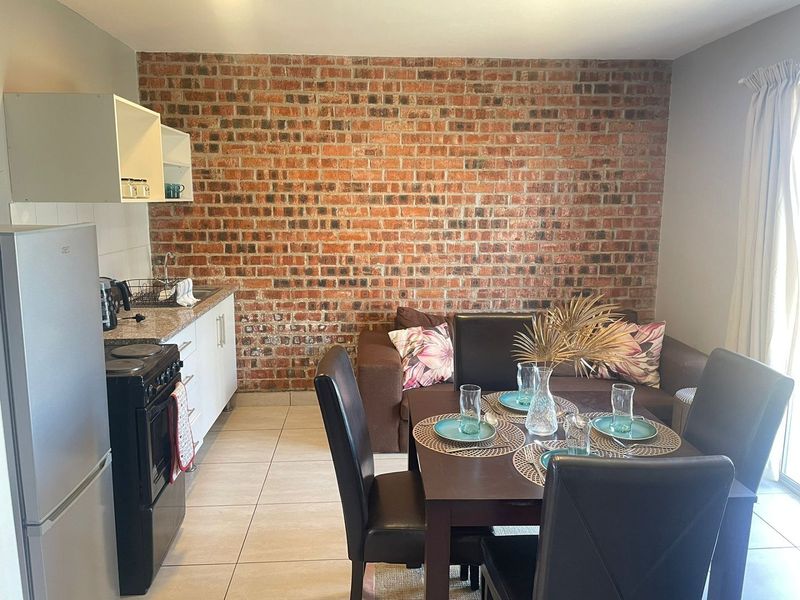 Open-plan living and kitchen area featuring a prominent exposed brick wall, tiled flooring, and functional kitchen cabinetry with a freestanding stove.