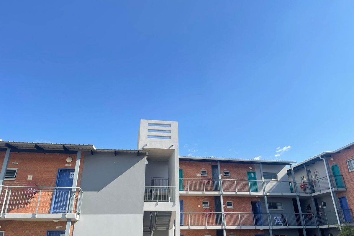 Exterior view of a multi-story apartment complex featuring exposed brickwork, external walkways with steel balustrades, and a central metal stairwell.