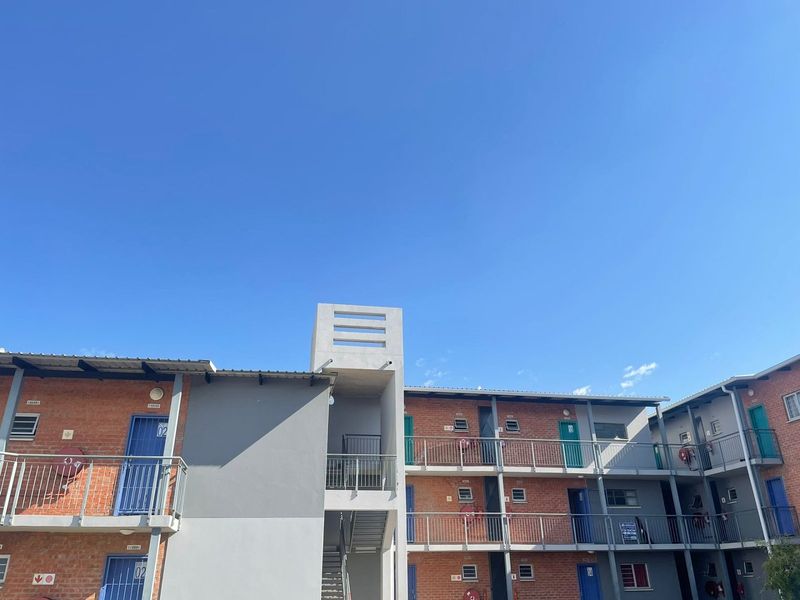 Exterior view of a multi-story apartment complex featuring exposed brickwork, external walkways with steel balustrades, and a central metal stairwell.