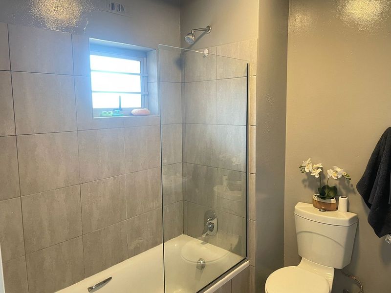 A clean, modern bathroom featuring a bathtub with a glass shower screen, tiled walls, and a standard toilet.