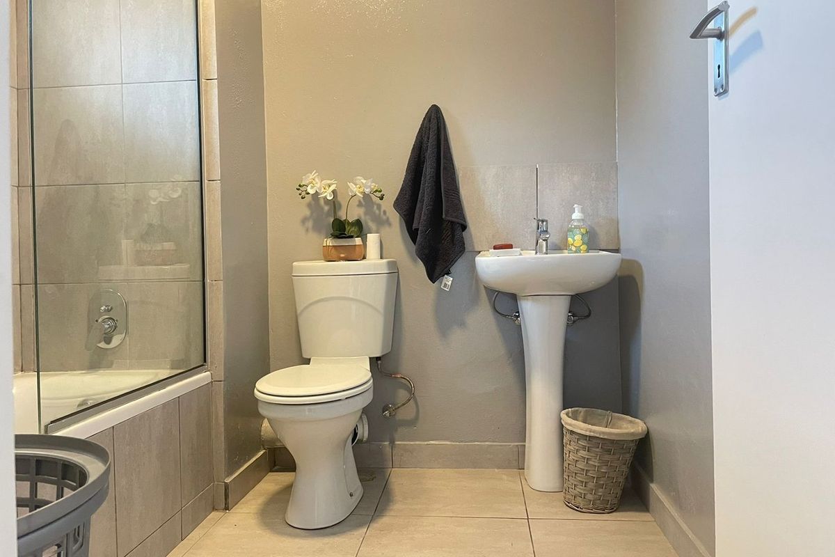 A functional bathroom featuring a pedestal basin, toilet, and a glass-enclosed shower with neutral wall and floor tiling.