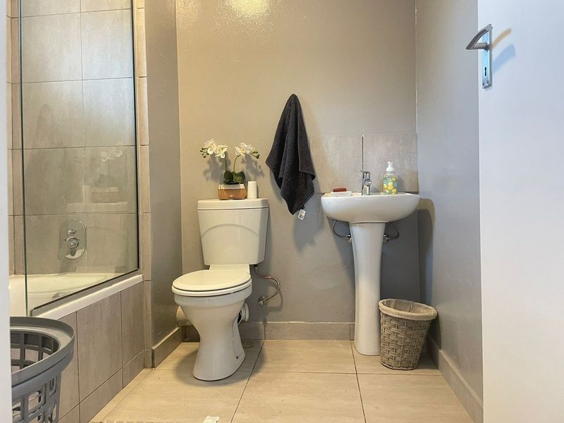 A functional bathroom featuring a pedestal basin, toilet, and a glass-enclosed shower with neutral wall and floor tiling.