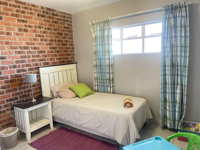 A bedroom featuring an exposed brick accent wall, tiled flooring, and a window with curtain fixtures.