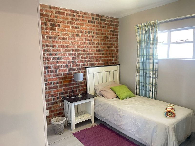 A cozy bedroom featuring an exposed brick accent wall, neutral tiled flooring, and natural light from a side window.