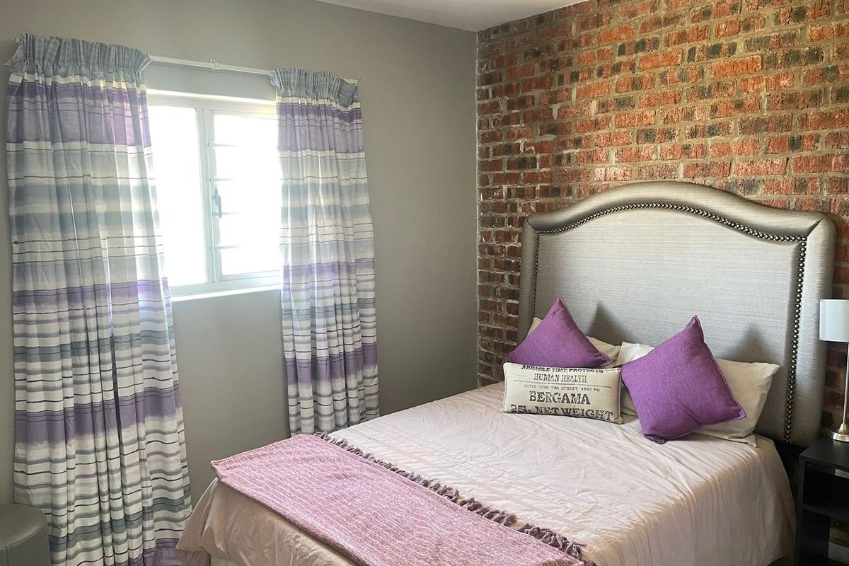 A cozy bedroom featuring a distinctive exposed brick feature wall and a window with natural light.
