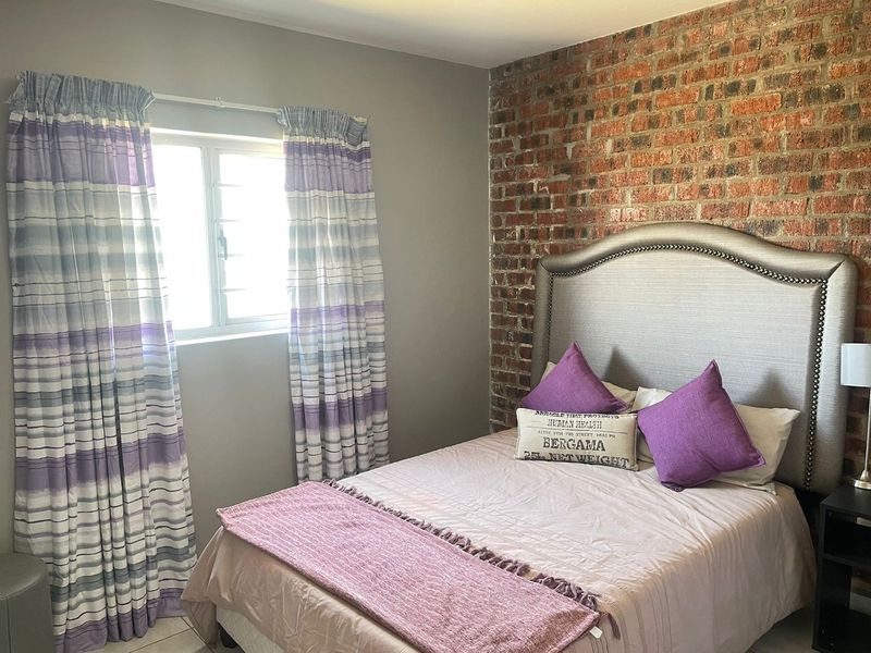 A cozy bedroom featuring a distinctive exposed brick feature wall and a window with natural light.