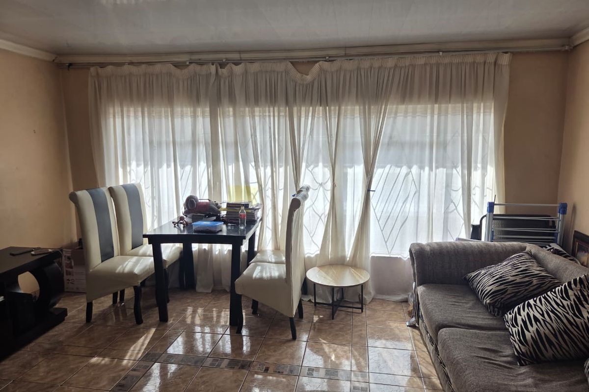 A living room area featuring tiled flooring and large windows covered by curtains, providing a functional space for relaxation and dining.