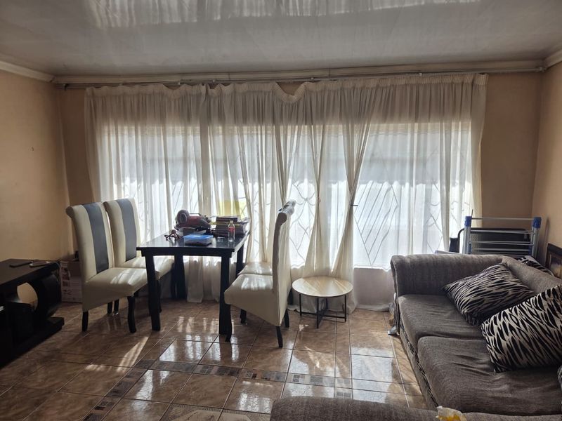A living room area featuring tiled flooring and large windows covered by curtains, providing a functional space for relaxation and dining.
