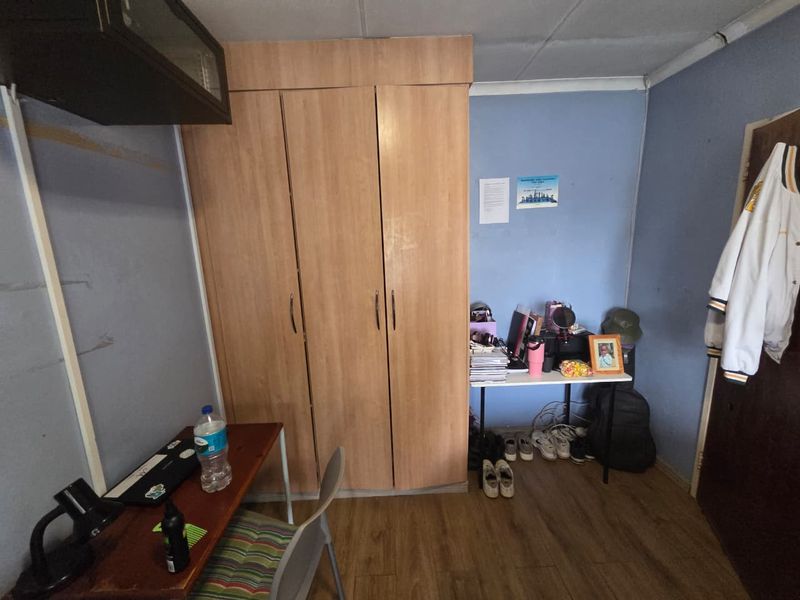 A bedroom featuring a built-in wooden wardrobe and laminate flooring, currently showing signs of wear on the walls and ceiling.