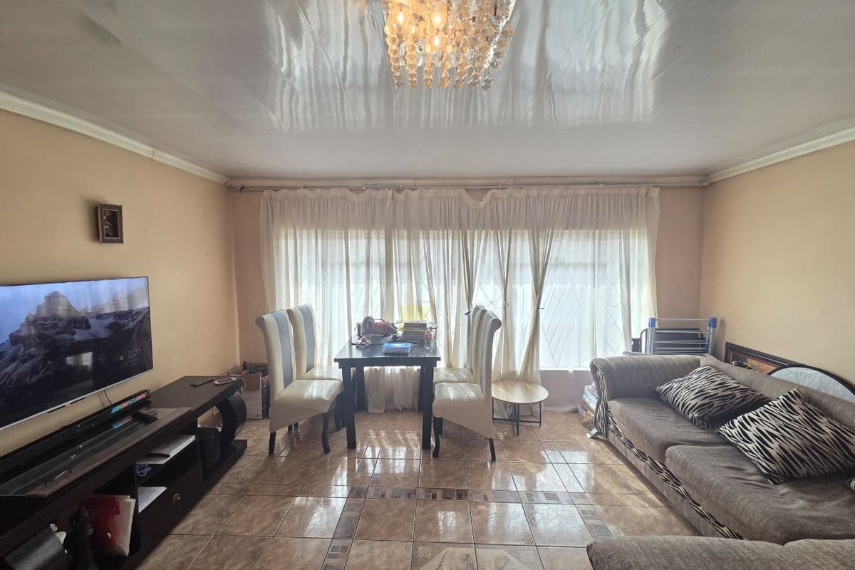 A living room featuring tiled flooring, a glossy ceiling finish, and a central crystal chandelier, offering a functional space for relaxation and dining.