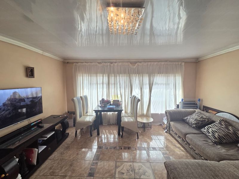 A living room featuring tiled flooring, a glossy ceiling finish, and a central crystal chandelier, offering a functional space for relaxation and dining.