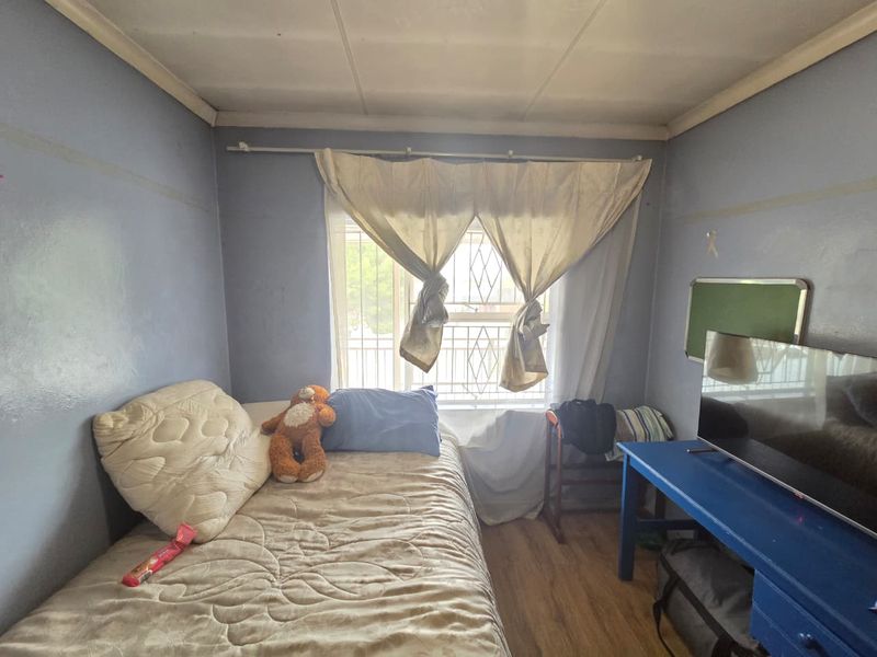 A compact bedroom featuring laminate flooring, a window with a security gate, and blue painted walls in need of cosmetic attention.
