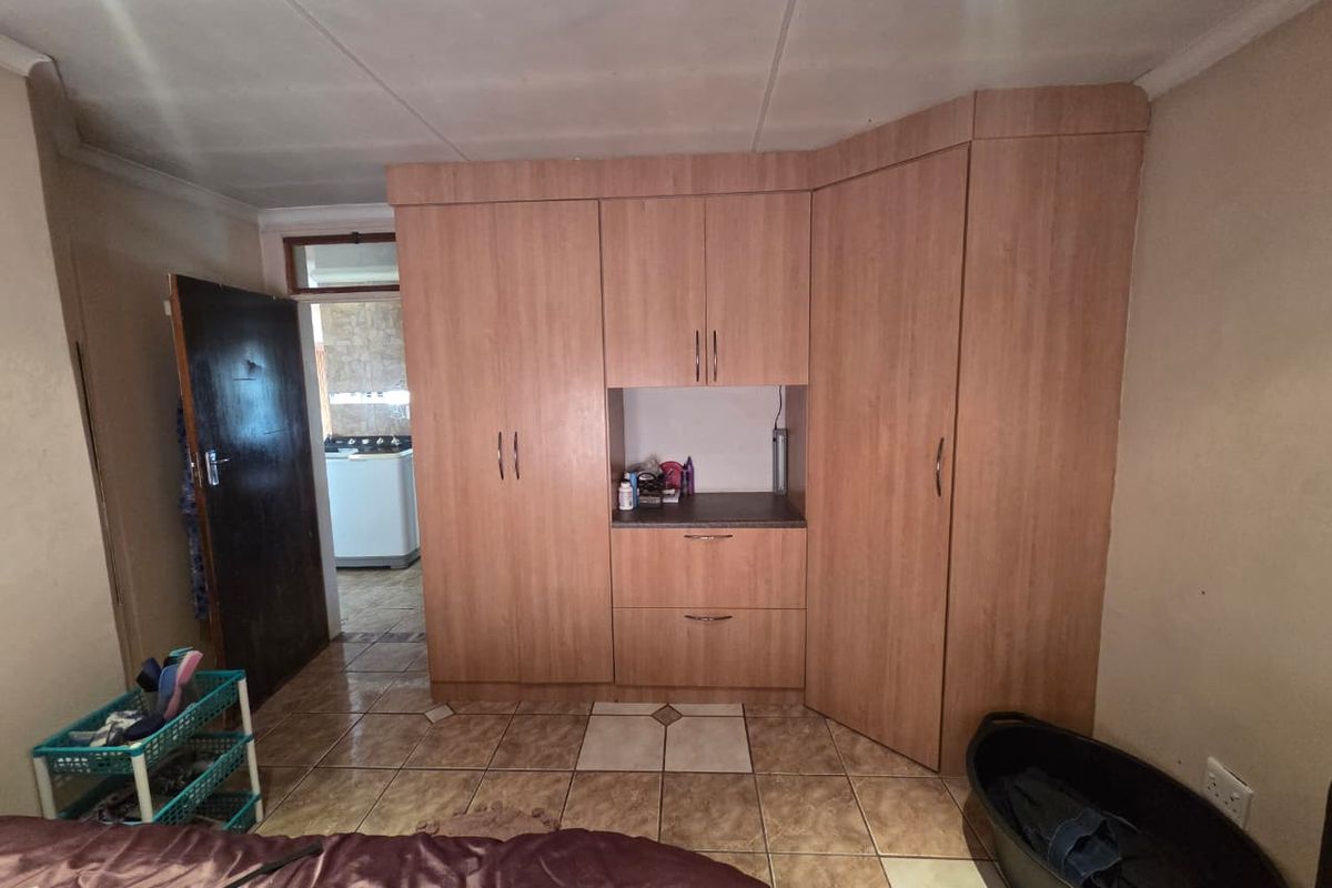 Bedroom featuring built-in wooden cupboards and tiled flooring, with an adjacent view into a utility area.