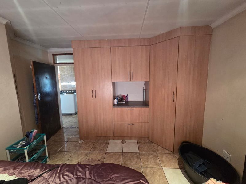 Bedroom featuring built-in wooden cupboards and tiled flooring, with an adjacent view into a utility area.