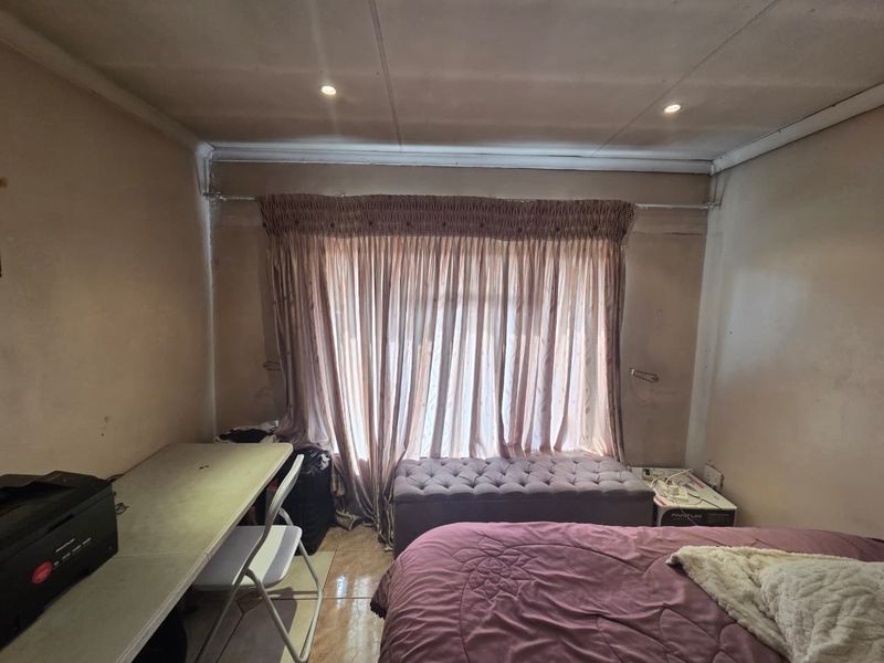 A bedroom featuring tiled flooring and recessed downlights, currently requiring cosmetic updates to the wall and ceiling finishes.