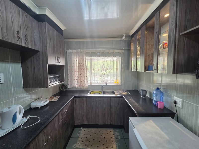 A functional kitchen featuring wood-look laminate cabinetry, dark granite countertops, a double basin sink, and tiled wall finishes with a security-gated window.
