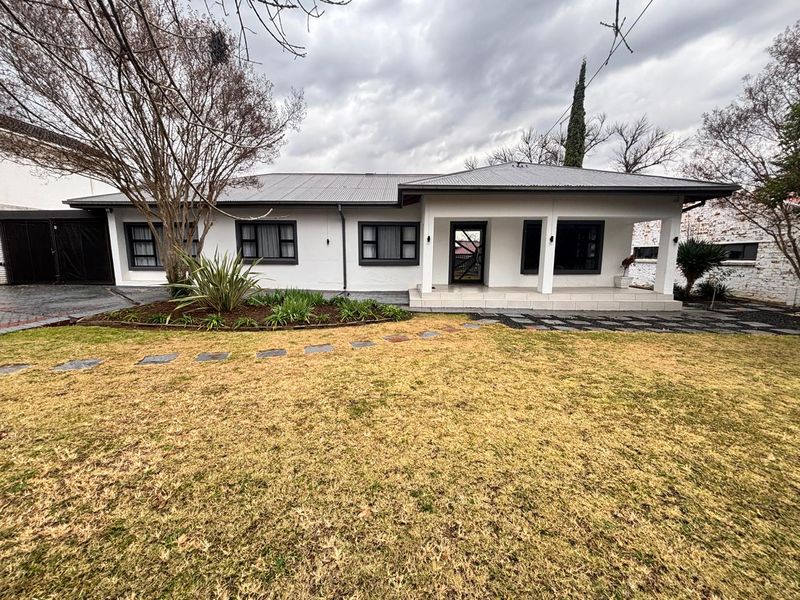 A well-maintained single-story house featuring a covered front patio, metal roofing, and a landscaped front garden with a stone pathway.
