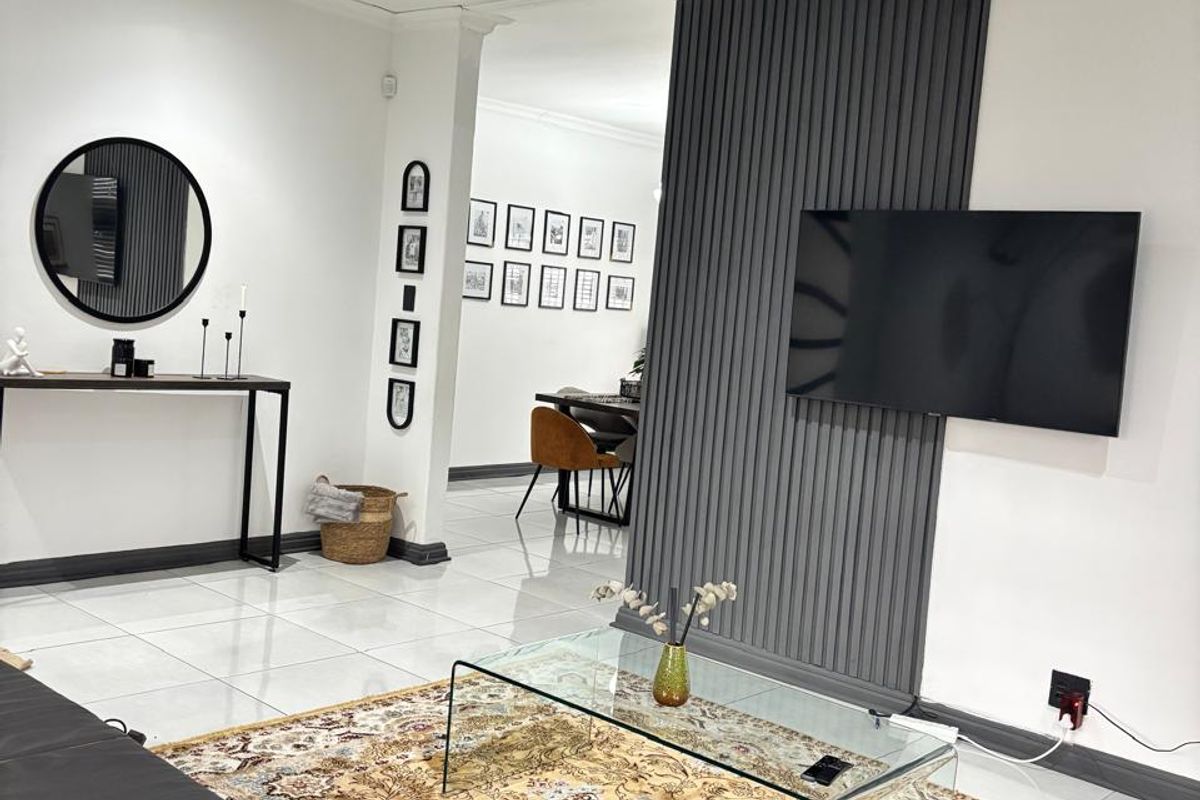 A modern living room featuring tiled flooring, recessed lighting, and a stylish dark grey decorative wall panel feature.