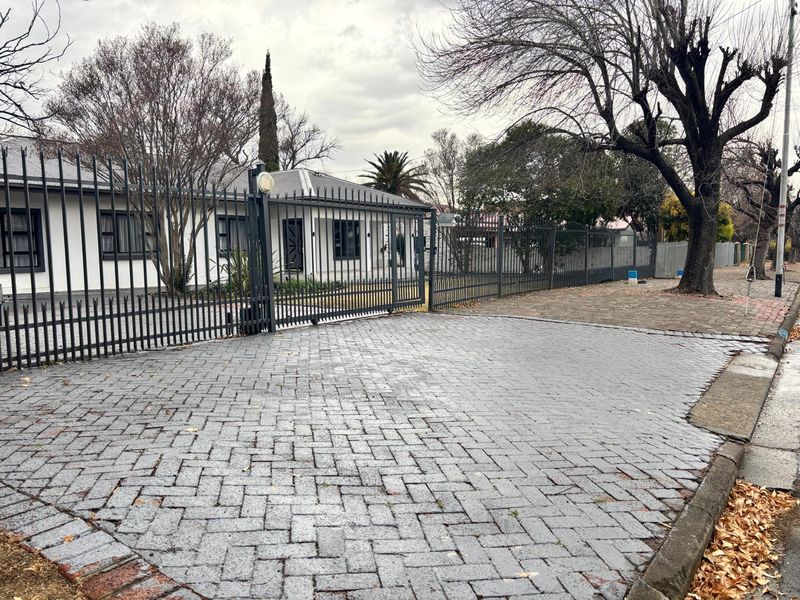 Front view of the property featuring a paved driveway, secure metal fencing, and a sliding gate leading to the main residence.
