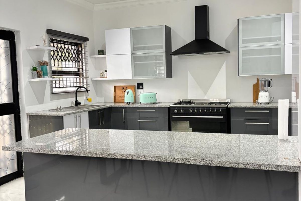 Modern kitchen featuring dark grey cabinetry, granite countertops, a central island, and high-quality built-in appliances including a gas hob and extractor fan.