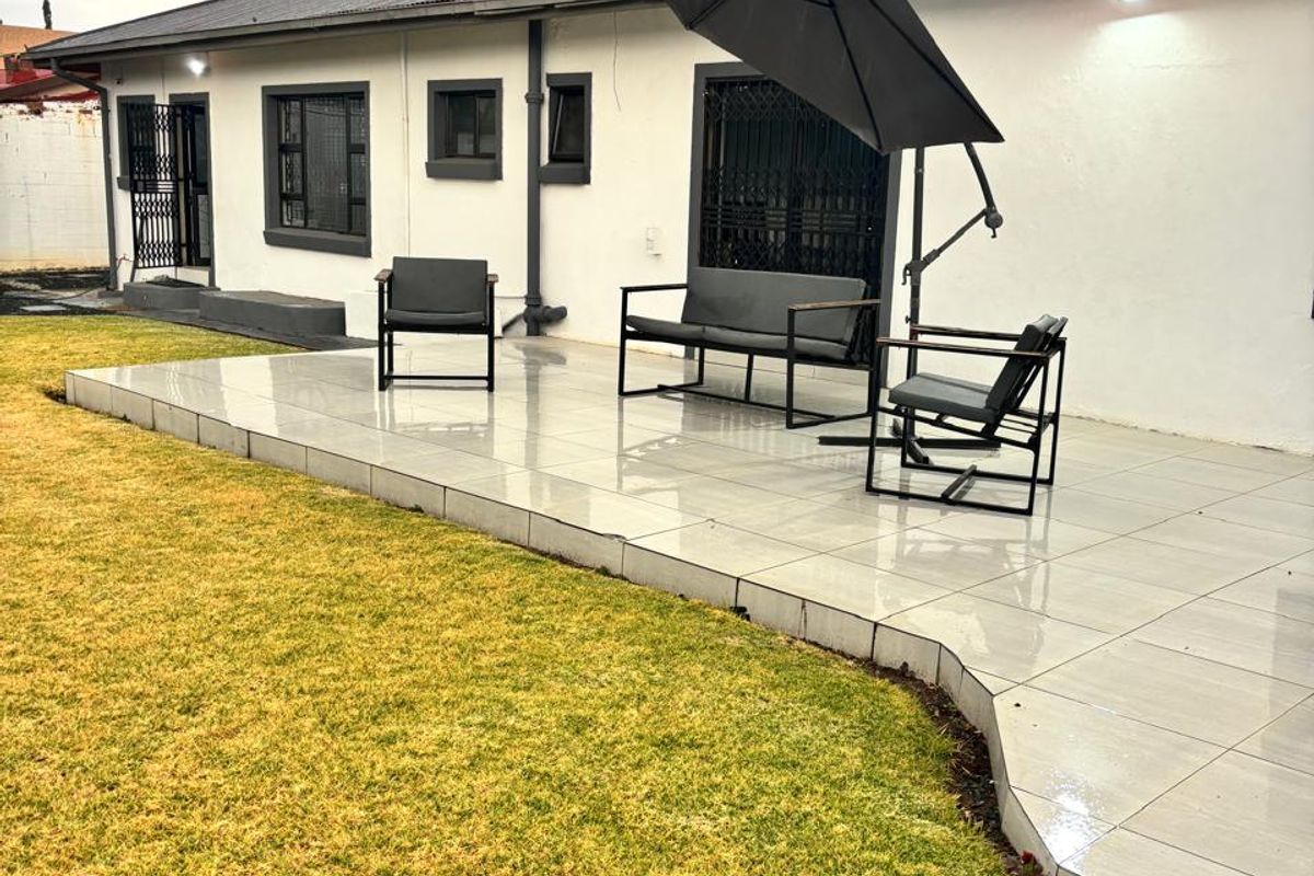 A well-maintained rear exterior featuring a tiled patio area, security gates, and a metal roof with a chimney.