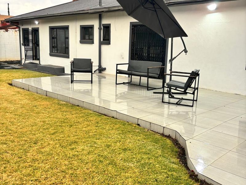 A well-maintained rear exterior featuring a tiled patio area, security gates, and a metal roof with a chimney.