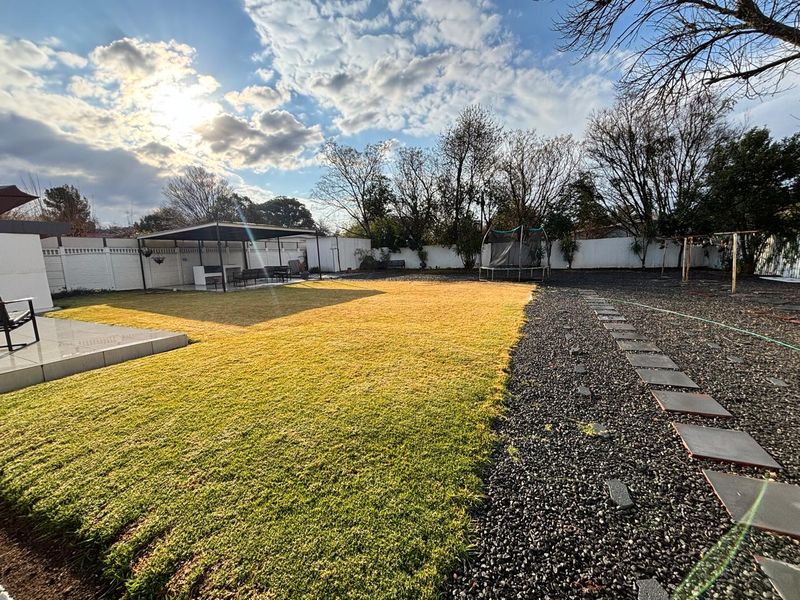 Spacious backyard featuring a manicured lawn, gravel pathways with stone pavers, and a covered patio area for outdoor entertaining.