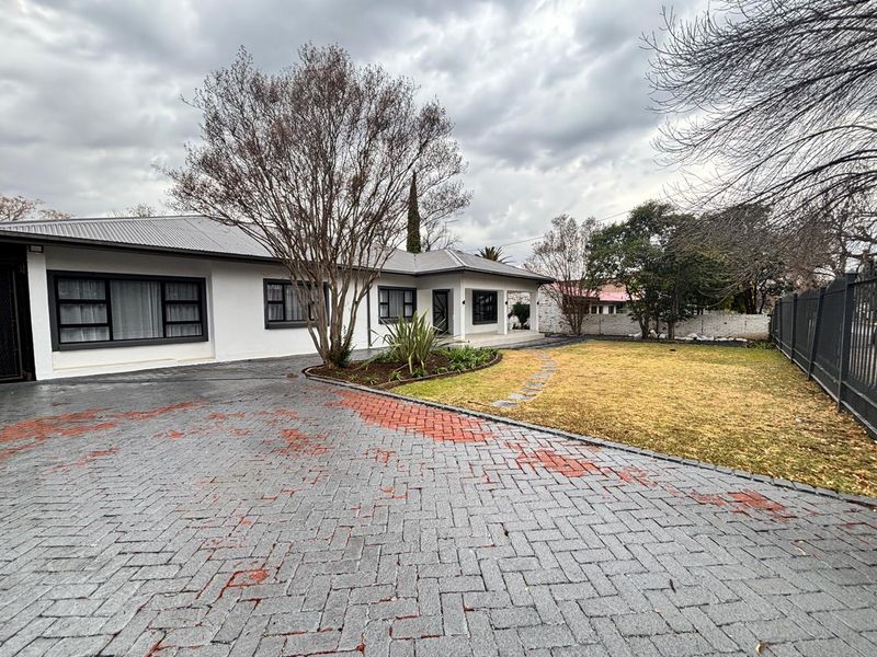 Front exterior view of a single-story house featuring a paved driveway, metal roofing, and established garden area.