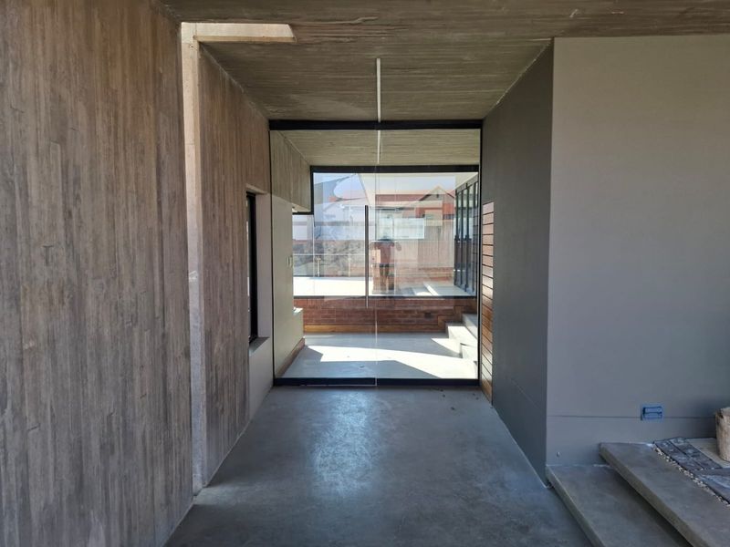 A modern, minimalist entrance hall featuring exposed concrete finishes, textured wall detailing, and a large glass pivot door leading to an outdoor area.