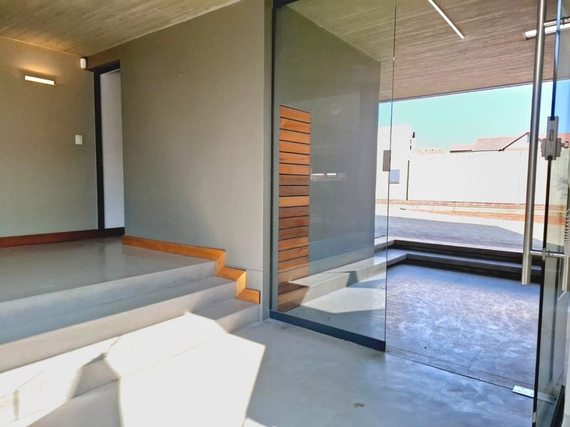 Modern entrance foyer featuring polished concrete flooring, exposed concrete ceiling, and a striking glass wall partition with timber accent detailing.
