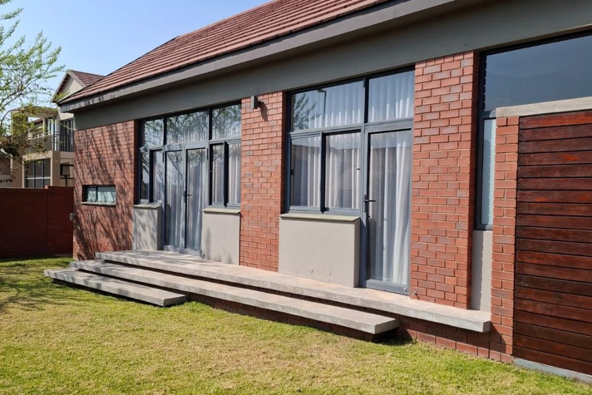 Rear view of a modern brick house featuring a tiled roof, aluminium-framed doors and windows, and concrete patio steps leading to a well-maintained lawn.