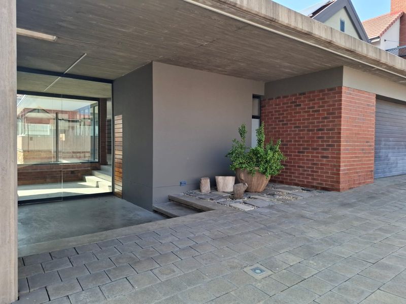 Modern front entrance featuring a concrete overhang, brick detailing, paved driveway, and large glass sliding doors leading into the home.