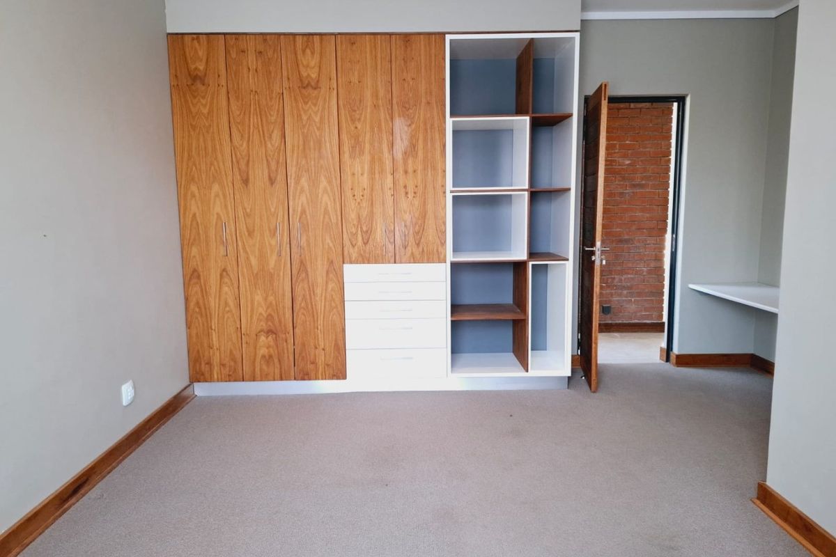 A spacious bedroom featuring extensive built-in wooden cabinetry, integrated shelving, drawers, and a fitted desk area with neutral carpeting.