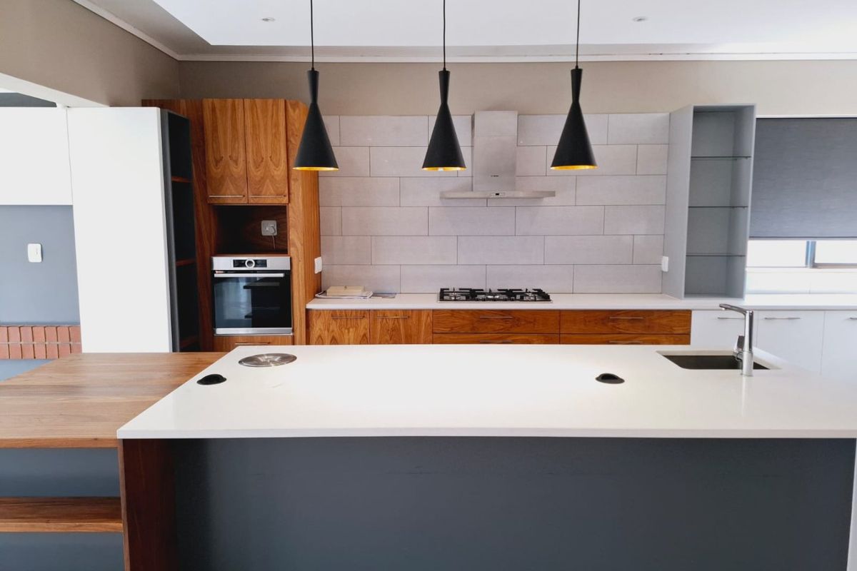 Modern kitchen featuring a large island, built-in oven, gas hob, extractor fan, and contemporary cabinetry with a clean subway tile backsplash.