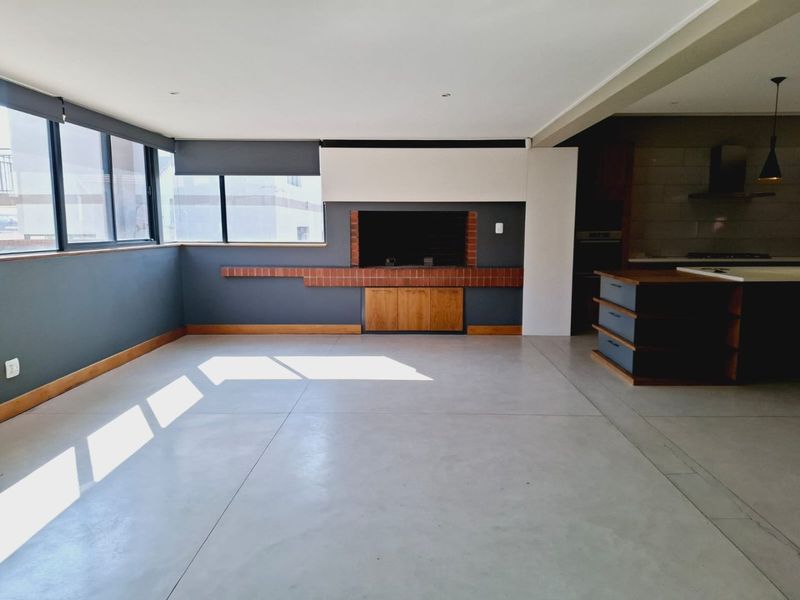 Spacious open-plan living area featuring polished concrete floors, a built-in fireplace with brick detailing, and a modern kitchen island with integrated cabinetry.