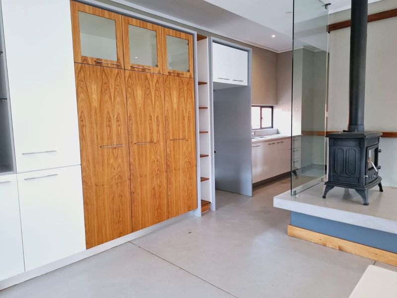 Modern open-plan living area featuring polished concrete floors, a sleek wood-burning fireplace with glass surround, and integrated cabinetry leading to a functional kitchen space.