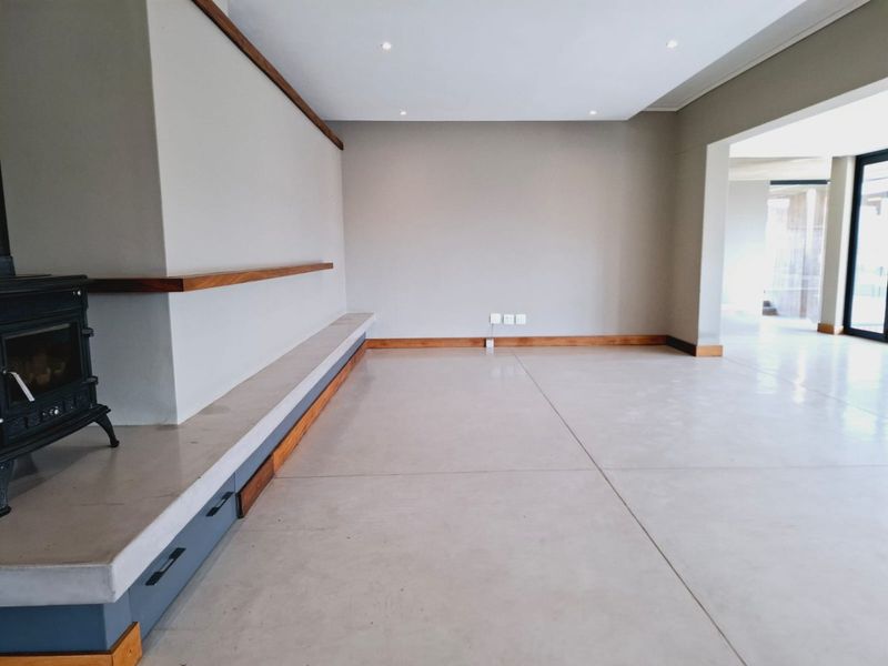 Spacious living area featuring polished concrete floors, a modern cast iron fireplace with a concrete hearth, and built-in timber shelving.