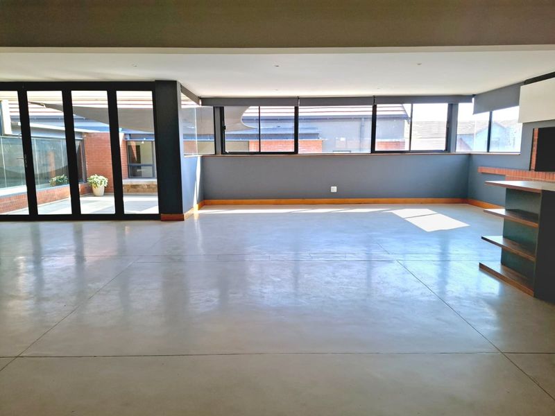 Spacious, light-filled living area featuring polished concrete floors, modern black aluminium window frames, and seamless access to an outdoor patio.