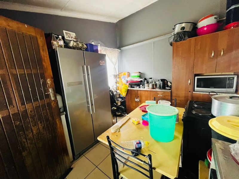 A compact kitchen area featuring built-in cabinetry, tiled flooring, and a built-in oven, currently utilized with various appliances and storage items.